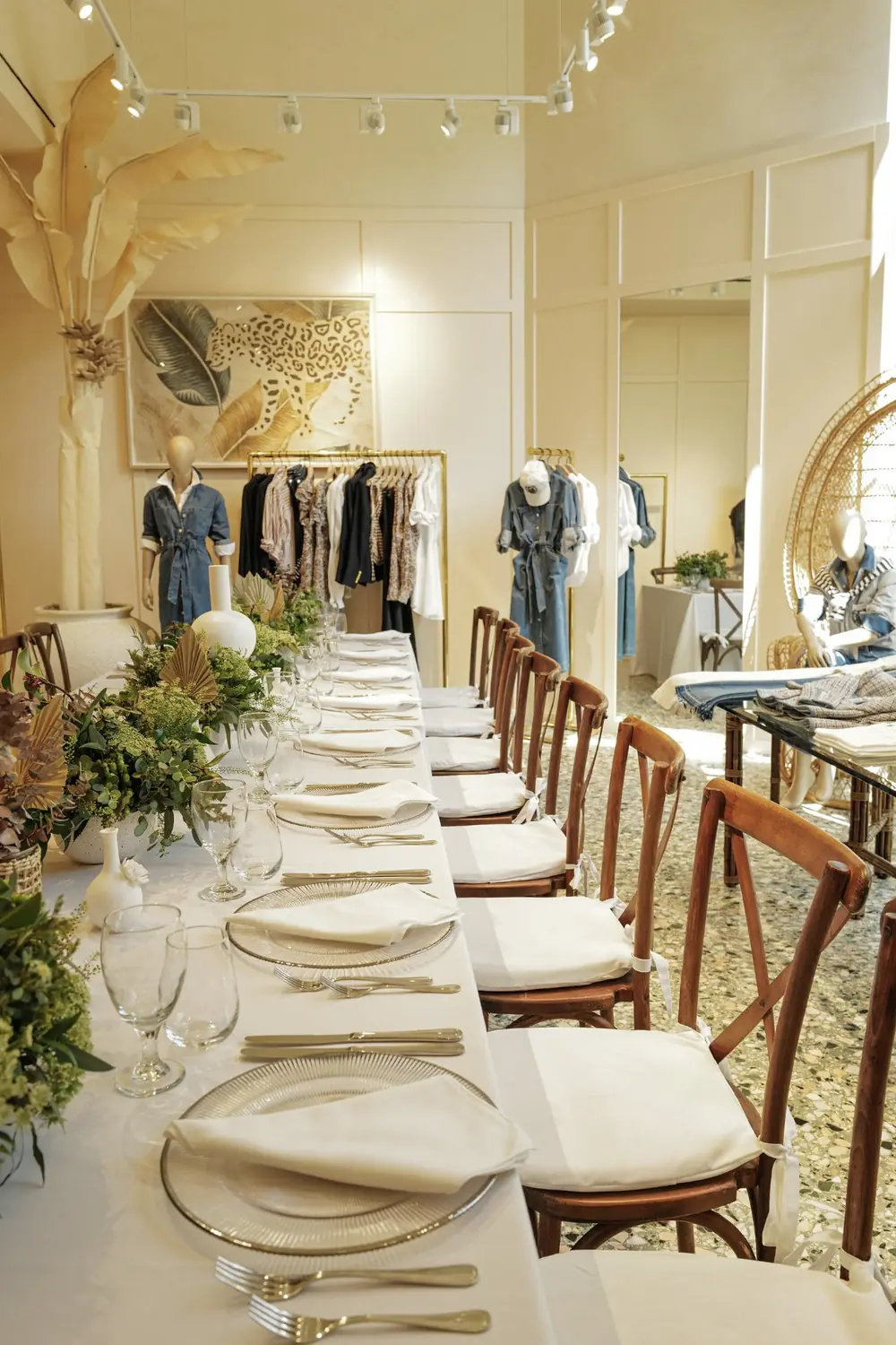 Long dining table set with white linens, glass chargers and wooden cross-back chairs for a private dinner